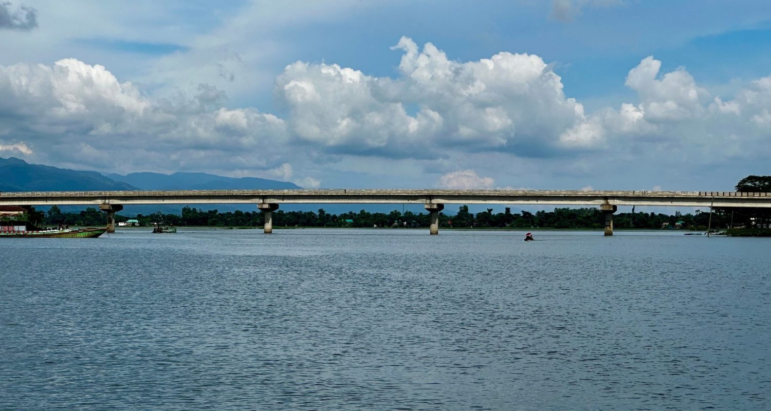Peaceful river scene with a bridge under a cloudy blue sky, ideal for travel and nature themes.